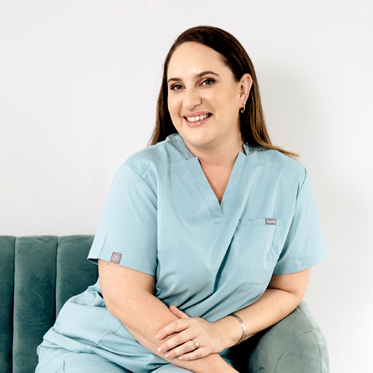 Aletia de Hahn, the Somatologist at Dr Hilla sitting in a green suede chair in her light turquoise scrubs.