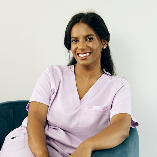 Shakeelah Kherekar, the skincare therapist at Dr Hilla, sitting in a green suede chair in her pink scrubs.